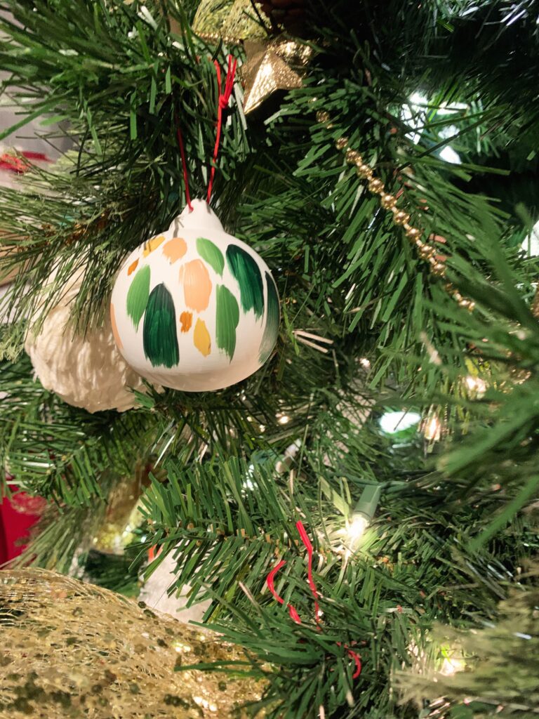 Gros plan sur une boule de Noël en céramique peinturée avec effet artistique, accrochée dans un sapin